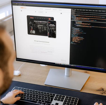 Mitarbeiter am Schreibtisch arbeitet an einem großen Monitor mit der ActiView-Website und einem Code-Editor.