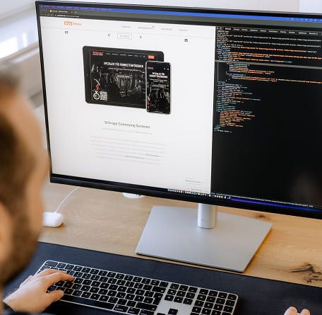Mitarbeiter am Schreibtisch arbeitet an einem großen Monitor mit der ActiView-Website und einem Code-Editor.