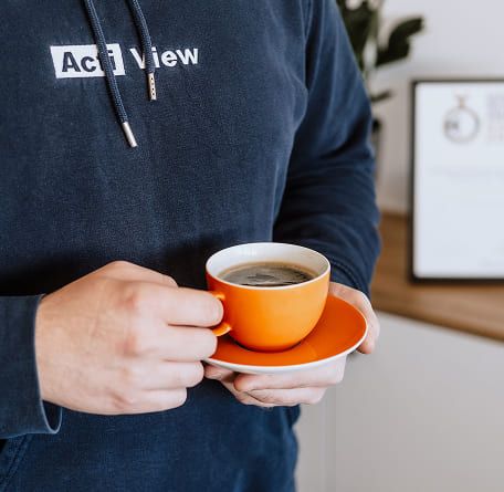 Mitarbeiter im ActiView-Hoodie hält eine orangene Kaffeetasse in den Händen.